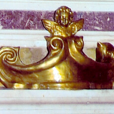 Il Cartiglio in creta misura 36x12 sormontato da un Angioletto a mezzo busto con le ali spiegate. Rifinitura in bronzo dorato. Il Cartiglio è posto sulla tomba del Sommo Pittore-Scultore viterbese Pietro Vanni dell'800